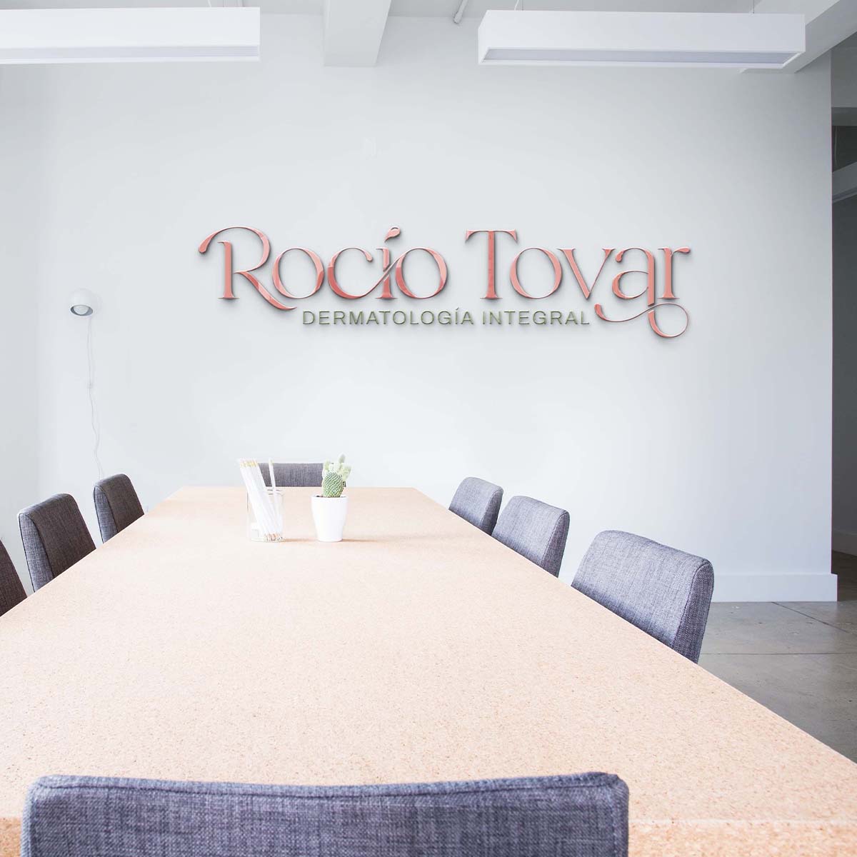 Logotipo de la Dra. Rocío Tovar impreso en la pared de una sala de juntas elegante con mesa de madera y sillas blancas.