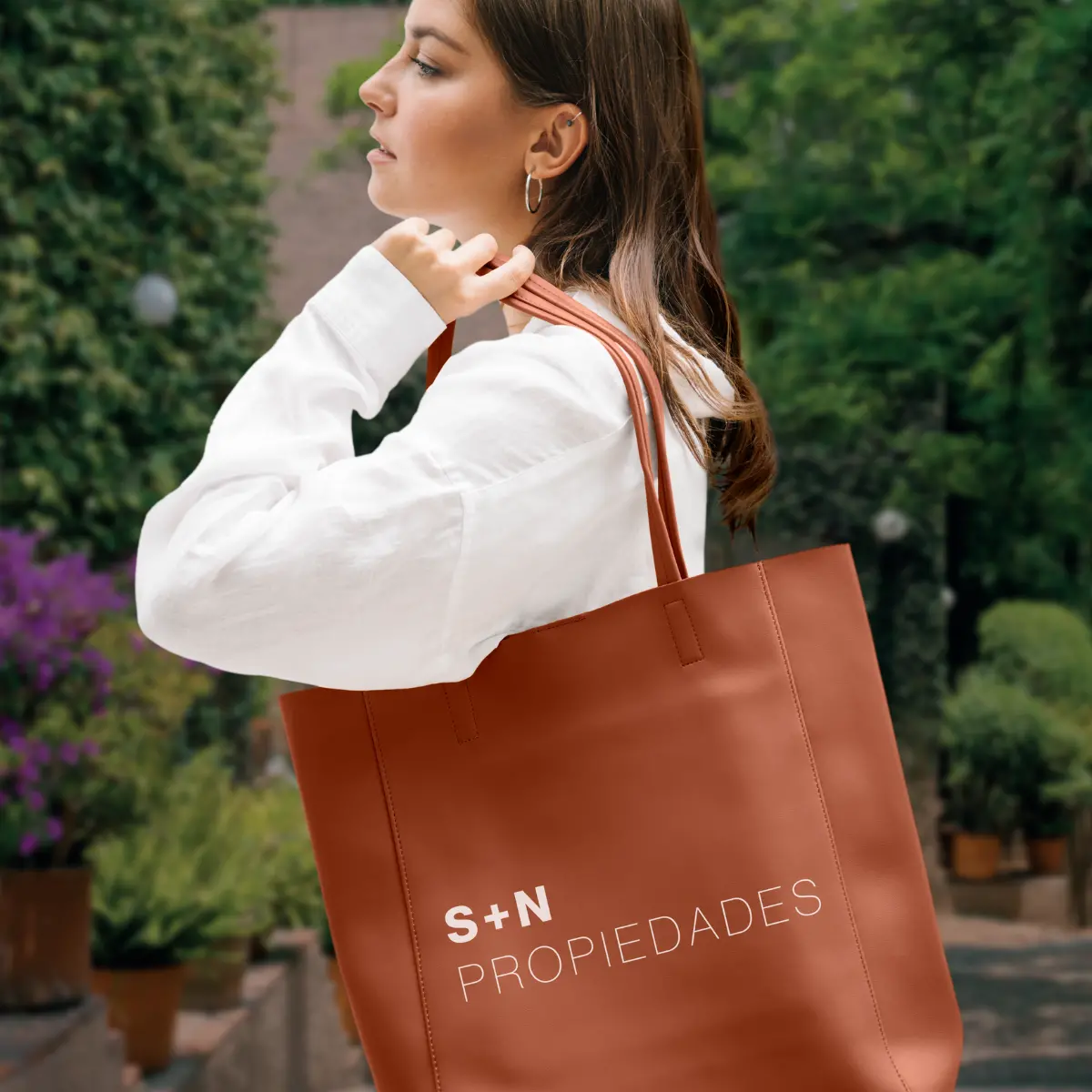 Mujer de perfil cargando una bolsa de cuero café, representando estilo ejecutivo e identidad de la marca S-N Propiedades.