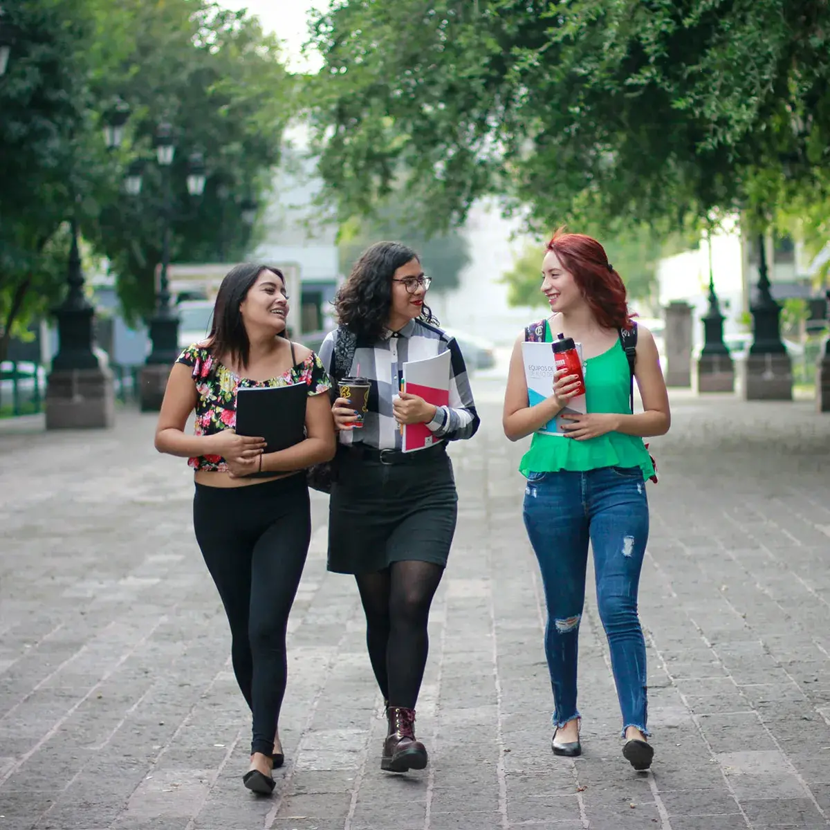 Tres mujeres jóvenes caminando y platicando al aire libre, practicando la tendencia de silent walking para el bienestar mental.