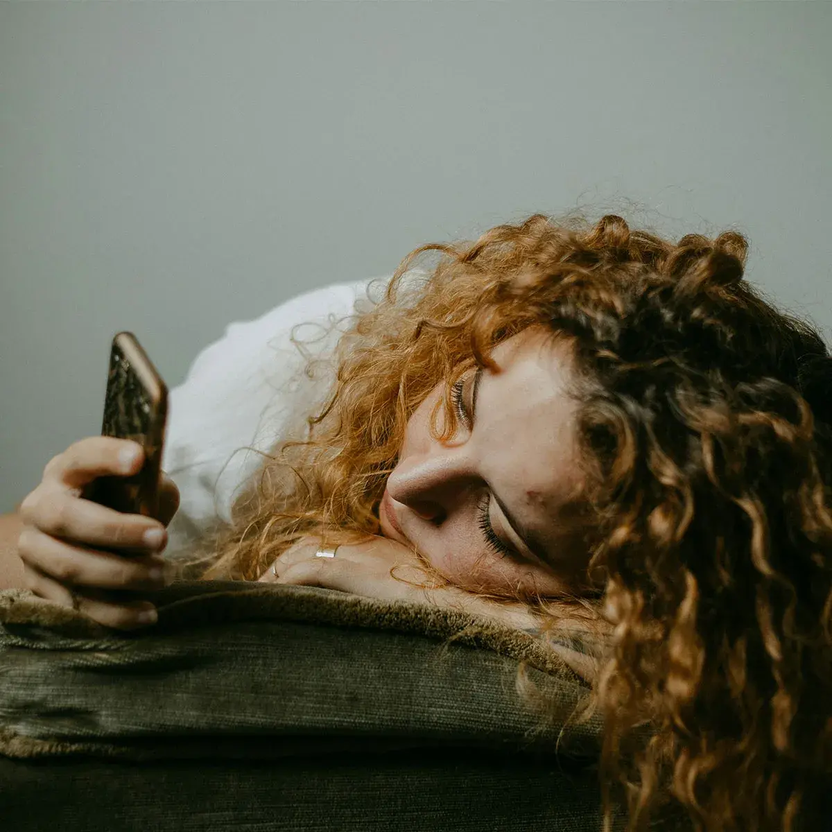 Mujer joven recostada cansada mirando su celular, representando el agotamiento digital y la fatiga mental en emprendedoras.