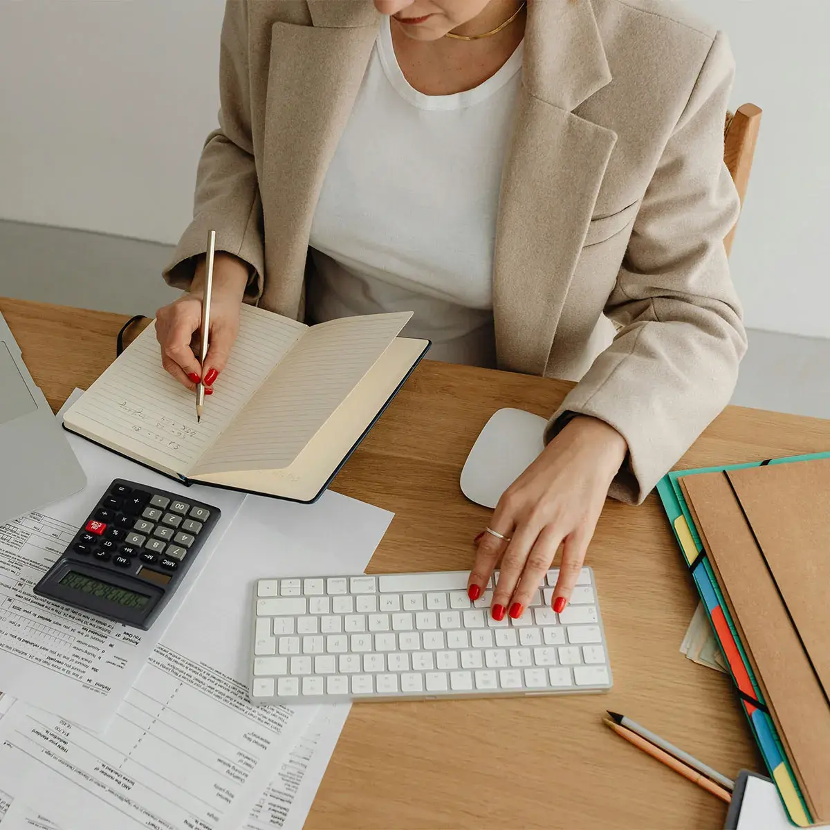 Primer plano de una emprendedora escribiendo en un cuaderno de contabilidad y usando un teclado de computadora en su escritorio, ilustrando el concepto de contabilidad circular.