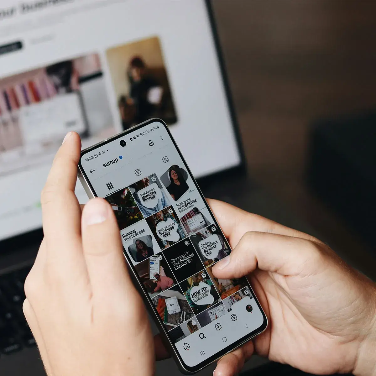 Persona sosteniendo un smartphone revisando un feed de Instagram con una laptop de fondo, concepto de de-influencing en redes sociales.