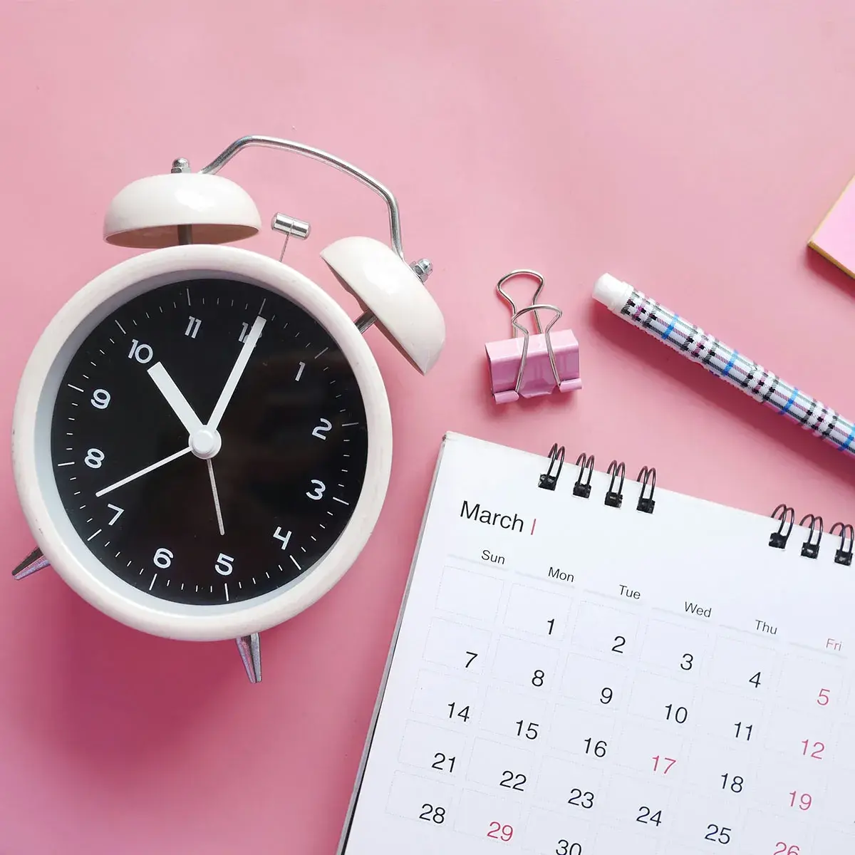 Reloj despertador blanco y calendario de escritorio para planificar y sincronizar tu calendario de Google con tu ciclo menstrual.