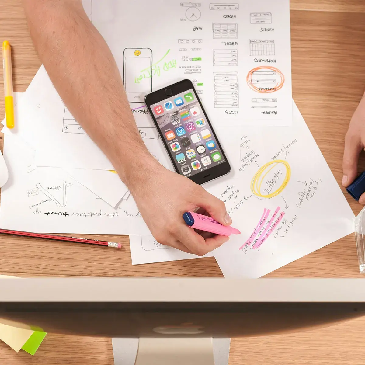 Manos trabajando en un plan de marketing de confianza con notas y dispositivos electrónicos sobre una mesa.