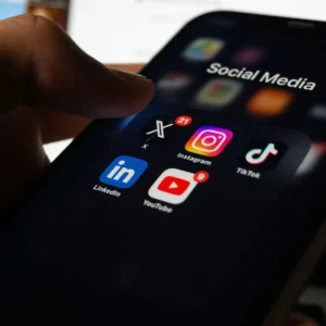 Mano sosteniendo un teléfono con iconos de redes sociales, representando la estrategia de curaduría extrema frente al exceso de contenido.